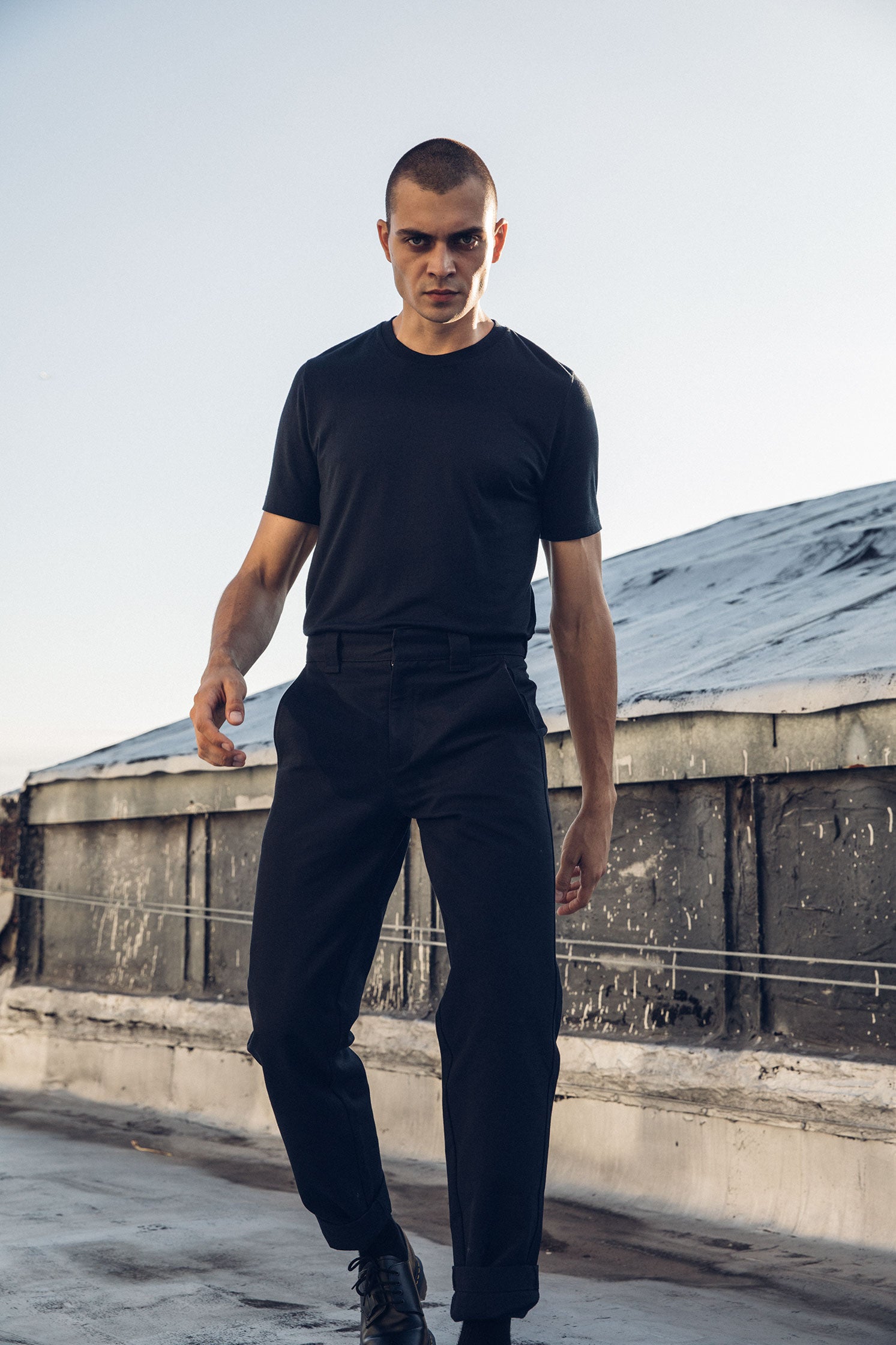 Kirill in the Washed Black Duckworks and a tucked in Black Ultrafine Merino Cut One T-Shirt, front view on a rooftop